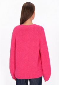 Przesadnie duży różowy sweter z okrągłym dekoltem, długimi rękawami i teksturowanym, puszystym materiałem. Brak widocznych wzorów lub akcentów.