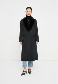 Pikk, kohandatud tumehall mantel pinstripe mustriga ja musta karusnahkadegaga kaelusega. Combiinatud lühikeste teksade ja mustade kontsaga mulesitega.