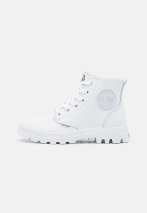 Botas altas blancas de material sintético con suela de goma texturizada, cierre con cordones y emblema circular en el lado.