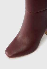 Βουργουνδί δερμάτινη μπότα μέχρι τον αστράγαλο με μυτερή μύτη και γυαλιστερή φινίρισμα. Ο σχεδιασμός διαθέτει υφή στην επιφάνεια και χαμηλό τετράγωνο τακούνι.