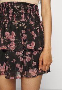 Svart blommig kjol med smockad midja. Har rosa och krämfärgade blommönster på lätt, genomskinligt tyg. Tva-lags volangdesign.