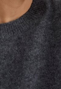 Mörkgrå stickad tröja med rund halsringning. Mjuk, texturerad tyg visar en blandning av fibrer och har en subtil lyster och lätt fluffighet.