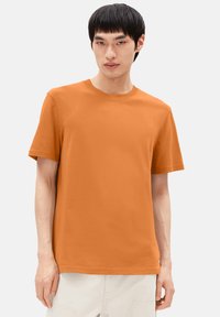 Kurze, orange Baumwoll-T-Shirt mit Rundhalsausschnitt und geradem Saum. Einfaches Design ohne erkennbare Muster oder Akzente.
