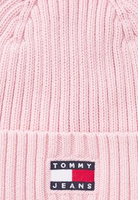 Roosa kudumüts, millel on ribakujundus ja volditud ääre. Sisaldab ristkülikukujulist sildikest, millel on "TOMMY JEANS" ja logo värvid sinine, valge ja punane.