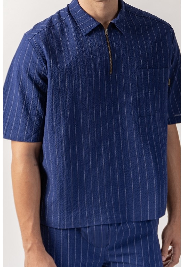 Námořnická pruhovaná košile s krátkým rukávem a zipem vpředu, vyrobená z texturované látky a s kapsou na prsou. Zpevněný límec a volnější střih.