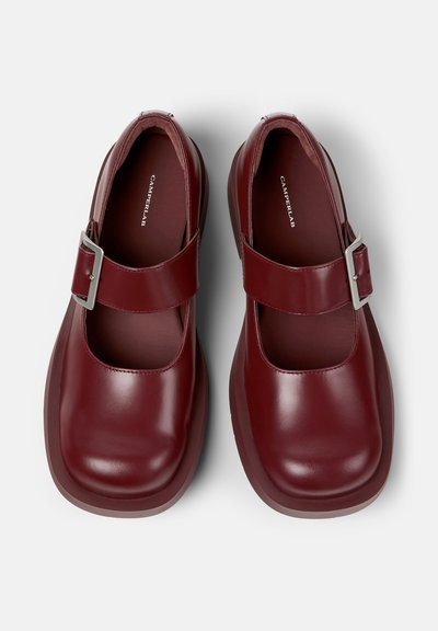 Paire de chaussures Mary Jane brillantes rouge foncé avec des bouts carrés et des larges brides maintenues par de grandes boucles argentées, vue de dessus.