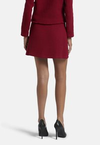 Rode gestructureerde blazer met bijpassende flared minirok, aangevuld met zwarte hoge hakken. Gezicht vanuit de achterkant, die details en pasvorm toont.