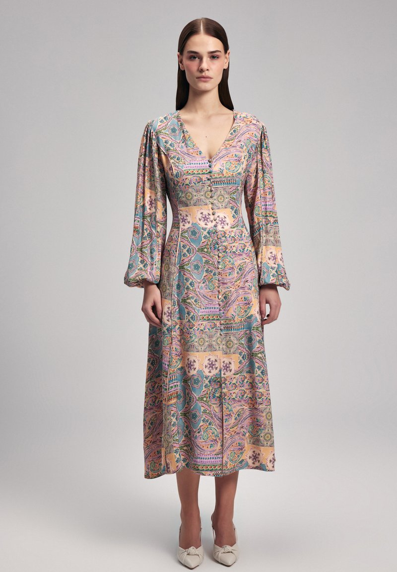 Abito a maniche lunghe in colori pastello, caratterizzato da una stampa paisley e floreale. Scollatura a V, dettagli con bottoni e gonna plissettata.