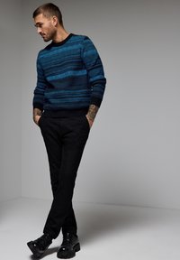 Suéter de punto con rayas horizontales en azul y marino, cuello redondo, puños acanalados, combinado con pantalones negros y botas negras resistentes.