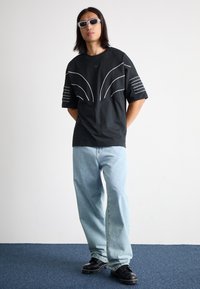 Black oversized t-shirt with white curved lines and stripes; paired with light blue jeans and black chunky shoes; gray sunglasses.