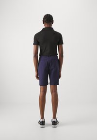 Polo de culoare neagră, cu mâneci scurte, asortat cu pantaloni scurți bleumarin. Îmbrăcămintea are o croială confortabilă și un design simplu, completată de adidași lejeri.