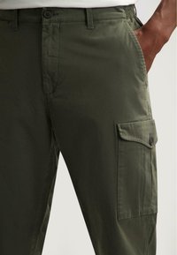 Olijf groene cargobroek met een knoopsluiting, zijzakken en een gestructureerde stof. Ontworpen voor comfort met een relaxte pasvorm.