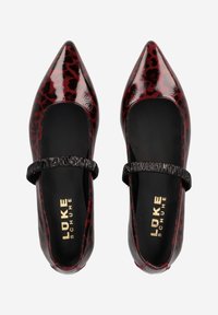 Ballerines Mary Jane en cuir verni rouge et noir avec des bouts pointus, présentant une sangle noire texturée sur le cou-de-pied et un léger motif léopard.