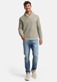 Suéter de punto verde claro con cuello de chal, combinado con jeans de mezclilla azul claros desgastados y zapatillas beige. La textura es gruesa y texturizada.