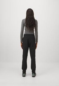 Harmaa pitkähihainen paita, joka on yhdistetty mustiin haalareihin, joissa on joustava vyötärö ja kapenevat lahkeet, käytettynä harmaiden ja mustien kenkien kanssa.