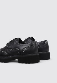 Schwarze Lederschuhe mit Nieten-Details, einer dicken strukturierten Sohle und einer abgerundeten Form. Verfügen über dekorative Nähte entlang der Ränder.