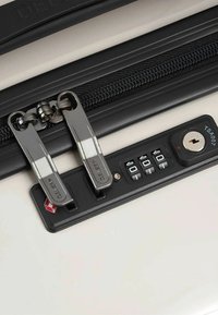 Cerniera della valigia Delsey con doppi cursori in cromo, che sicura il tessuto nero, dotata di un lucchetto a combinazione conforme alle norme TSA e di un foro per la chiave.