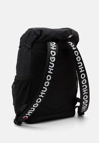 Zaino nero con materiale esterno morbido, pannelli in rete e spallacci con logo stampato. Presenta un design a chiusura arrotolata e dettagli testurizzati.