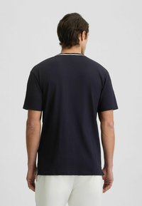 Námořnická modrá tričko s krátkým rukávem a kulatým výstřihem, hladký povrch a kontrastní lemování podél límce. Minimalistický design.