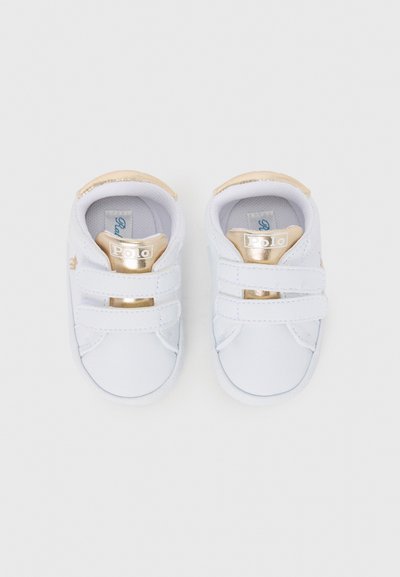 Baskets blanches pour bébés avec une surface lisse, accents dorés sur les sangles et le talon, dotées de fermetures à scratch et d'une forme de chaussure à bout arrondi.