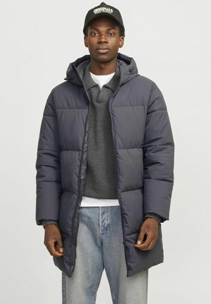 Marineblå pufferjakke med hætte, quiltet design og frontlommer, båret over en grå sweater. Sammen med lyseblå denimjeans.