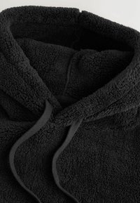Juodas vilnonis hoodie su minkšta tekstūra, sutrauktu kaklu ir atitinkamais raiščiais. Dizainas sutelktas į šilumą ir komfortą.