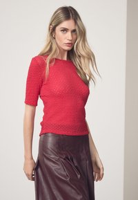 Crvena teksturirana majica s kratkim rukavima, uskog kroja. Uparena s visokim strukom bordo kožnom suknjom s okomitim prugama.