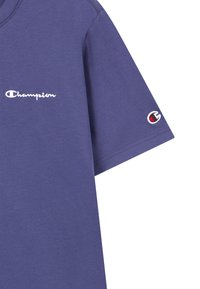 Paarse katoenen t-shirt met korte mouwen. Bevat het "Champion" logo in het wit op de borst en een klein geborduurd logo op de mouw.