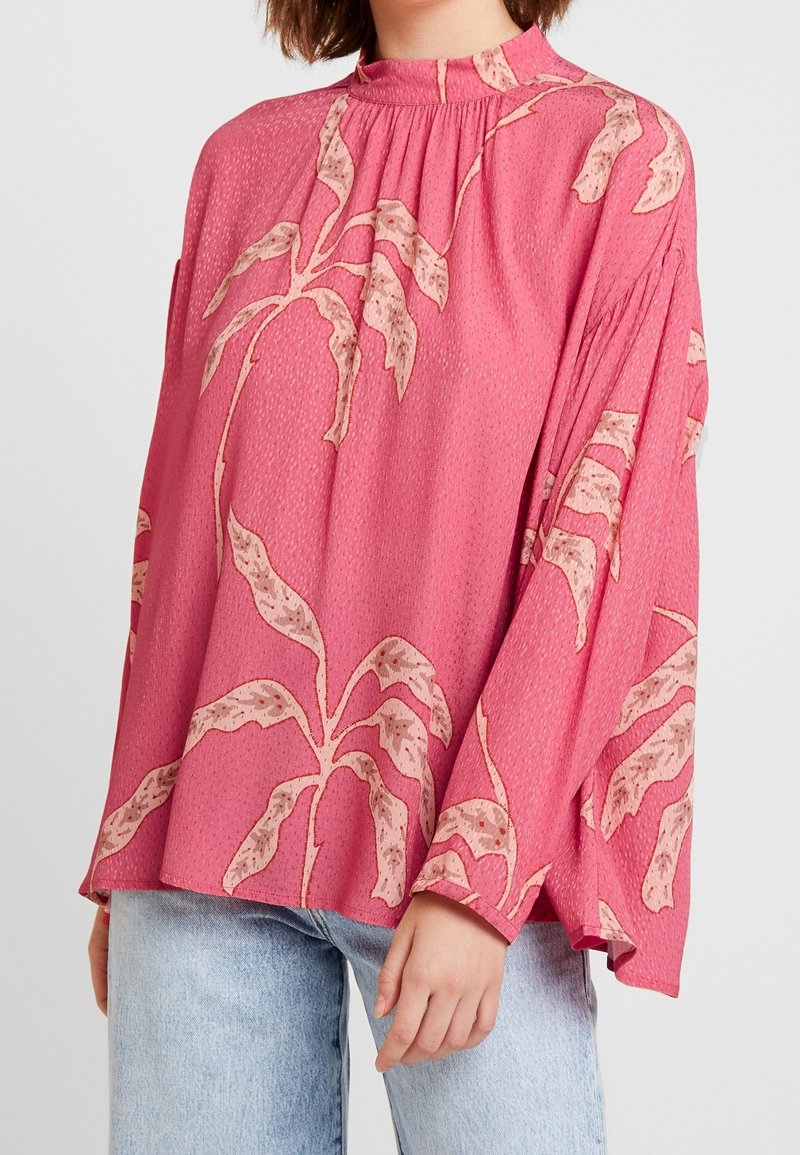 Rosa långärmad blus med hög hals, i en texturerad tyg och ett botaniskt lövmönster i beige. Lätt passform med vida ärmar.