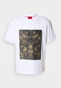 Weißes Baumwoll-T-Shirt mit einem quadratischen, dunklen Blumenmuster, das goldene Akzente und Vogelmotive aufweist. Label "HUGO" oben im Design.