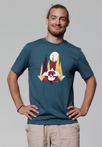 Teal katoenen t-shirt met een grafisch ontwerp van geometrische vormen in bordeauxrood, geel en wit. Korte mouwen en ronde hals.