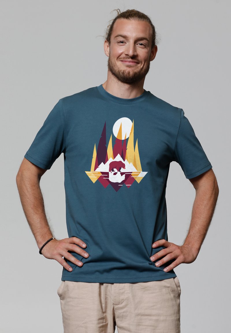 Teal katoenen t-shirt met een grafisch ontwerp van geometrische vormen in bordeauxrood, geel en wit. Korte mouwen en ronde hals.