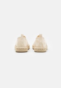 Espadrilles de lona beige con suela de yute, que presentan un diseño sencillo y una cinta trasera para facilitar el calzado. Forma plana y redondeada.