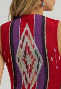 Rode mouwloze trui met een geometrisch patroon in paars, wit en groen; textuurgebreide stof met contrasterende strepen aan de zijkanten.