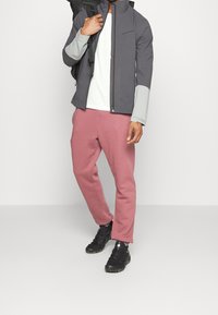 Grijze lichtgewicht jas met contrasterende lichtgrijze mouwen, wit T-shirt, roze sweatpants en zwarte schoenen. Eenvoudige, functionele buitenkleding.