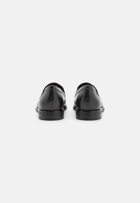 Zapatos de cuero negro con un acabado suave, punta redondeada, tacón bajo y detalles de costura sutiles en la parte superior. Diseñados para ocasiones formales.