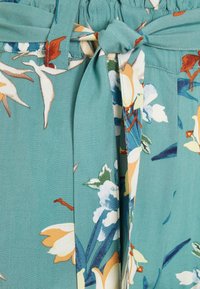 Tealtyg med blommönster som har vita, orange och gröna blommor, knytet i midjan med synliga sömmar.