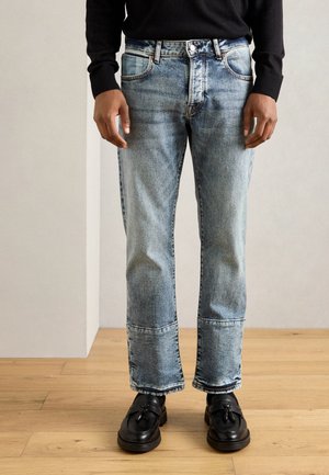 Lysblå denimjeans med en avslappet passform, som har whiskeringdetaljer, synlige sømmer og en rett ben-design. Svart teksturert sko blir brukt.