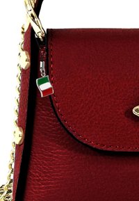 Rode leren handtas met een gestructureerde afwerking, gouden hardware en een sleutelhanger met de Italiaanse vlag. Aan de tas is een kettinghengsel bevestigd.