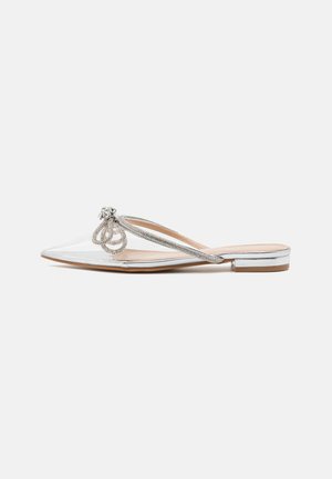 Chaussures transparentes à bouts pointus, faciles à enfiler, avec des accents métalliques argentés et un nœud décoratif sur le dessus. Talon plat.