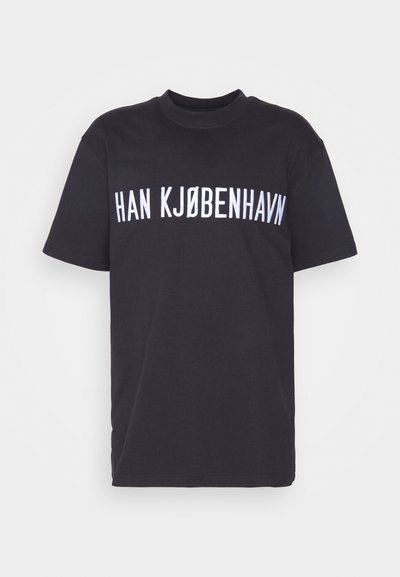 Melna kokvilnas T-kreklu ar apaļu kakla izgriezumu, uz kuras krūtīm ir uzraksts "HAN KJØBENHAVN" treknā baltā burtnīcā. Īsas piedurknes.