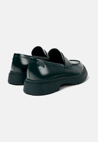 Mörkgröna sneakers med blanka läderdetaljer, rundad form, tjock svart sula och diskret logotyp på hälen.