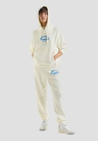 Felpa con cappuccio e pantaloni jogger coordinati, realizzati in tessuto morbido, con testo grafico blu. Cappuccio con coulisse e polsini a coste.