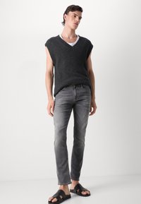 Maglione senza maniche grigio scuro a maglia con scollo a V, jeans grigi aderenti e sandali neri scivolati. Design semplice con finitura testurizzata.