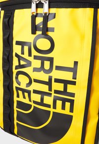 Zaino giallo con logo nero "THE NORTH FACE", dotato di un'esterno liscio e resistente, due tirazip argento e dettagli neri sui lati.