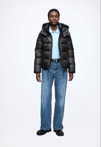 Fekete kapucnis pufi dzseki, steppelt textúrával; világoskék galléros póló; bő fazonú világos farmernadrág; fekete masszív cipők.