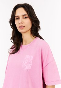Oversized roze katoenen t-shirt met een textuurontwerp op de borst met het woord "PROTEST" en abstracte patronen. Korte mouwen, ronde hals.