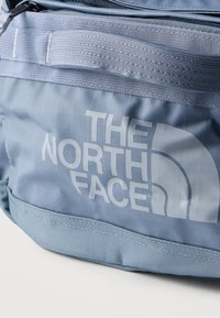 Τσάντα από ανοιχτό μπλε ύφασμα με ραμμένη λαβή και λευκό λογότυπο "THE NORTH FACE" στην μπροστινή πλευρά, σε λευκό φόντο.
