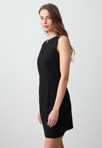 Abito nero senza maniche con silhouette aderente, tessuto morbido, scollatura a occhiello e dettagli sottili sulla seam frontale.