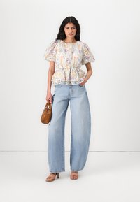 Blomstrete peplum-top med puffede ermer i myk stoff, kombinert med vide jeans. Tilbehøret inkluderer en liten brun håndveske og sandal med stropper.